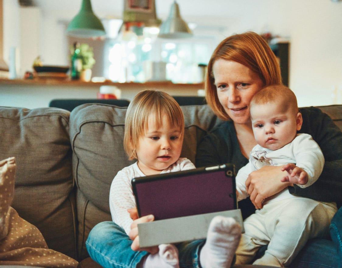 Family of three sat on a sofa watching an ipad.