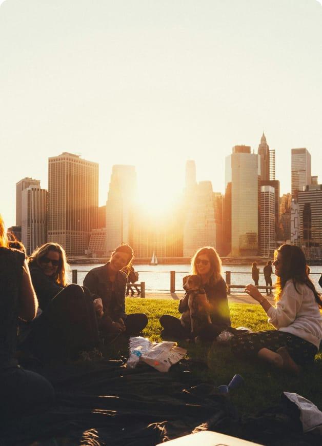 Group of people sat in the park, with a sunset falling over the city