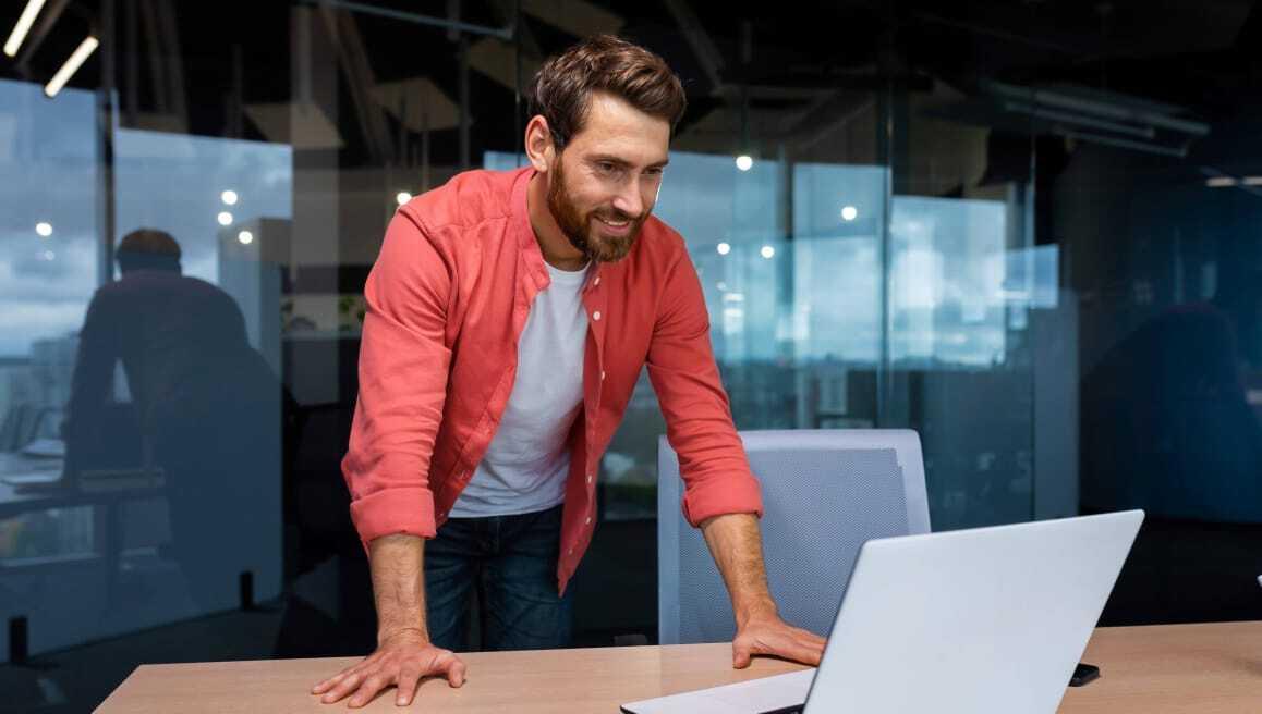 Man in a red open shirt, leaning on a table with a laptop