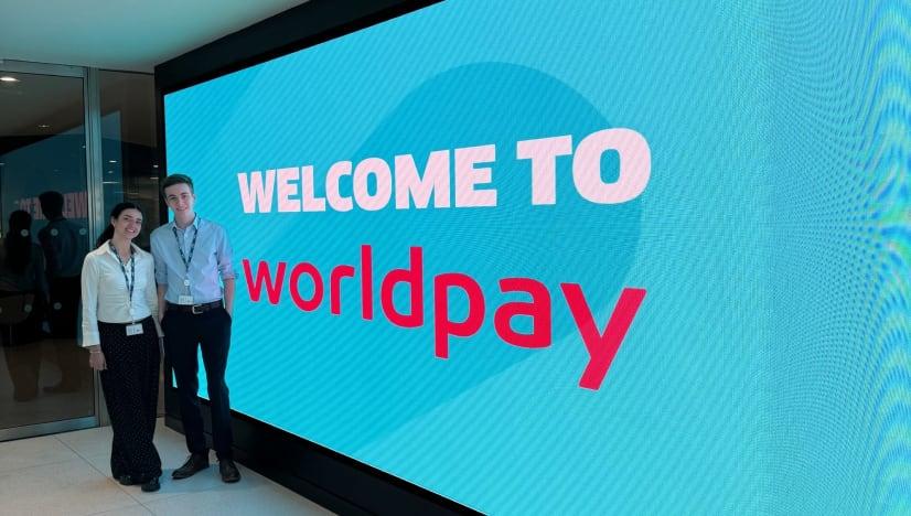 Two people stood infront of a welcome screen with the text Welcome to Wolrpday.